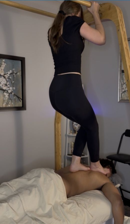 Mariah holding the bamboo bars with her feet on a client's upper back